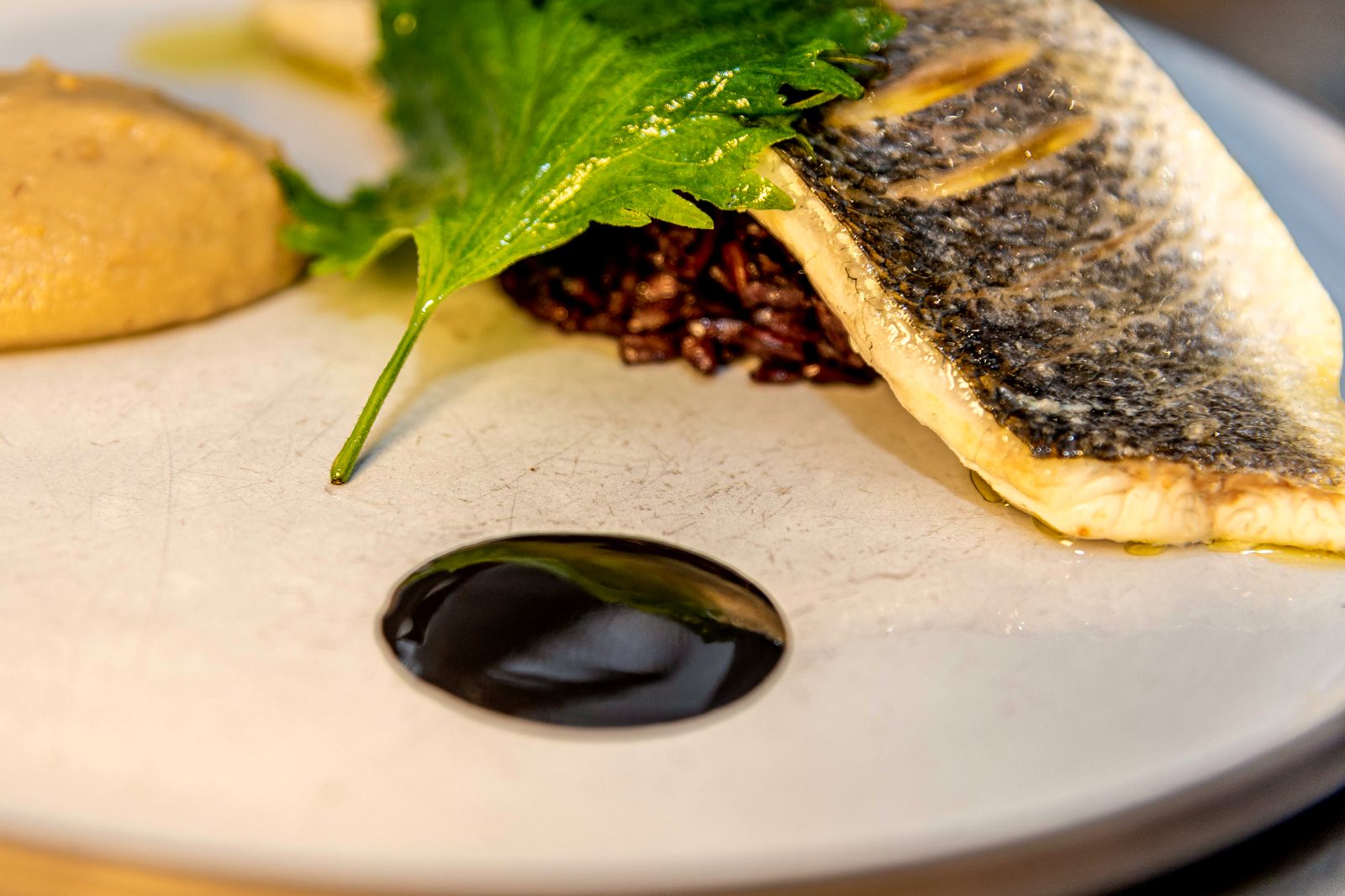 Le Bar de L’Apibo : filet à la peau striée sur riz noir vénéré, feuille de shiso et sauce laquée, plat signature du chef Anthony Boucher à Paris