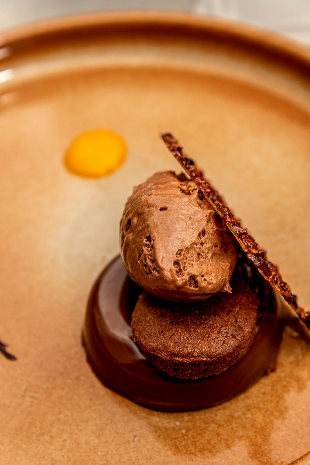 Le Chocolat de L’Apibo dressé à la verticale : mousse, ganache et tuile de grué de cacao sur assiette ocre, dessert signature à Paris 2e