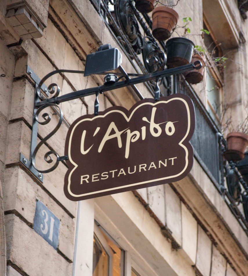 Enseigne suspendue du restaurant L’Apibo en fer forgé au 31 rue Tiquetonne à Paris 2e, lettres crème sur fond brun au-dessus de la façade en pierre