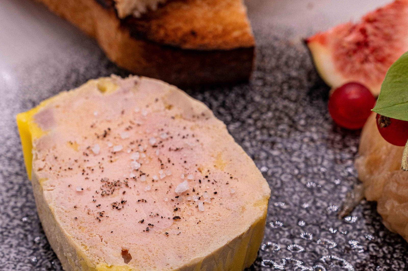 Foie gras de L’Apibo poivré et fleur de sel, pain toasté, figue fraîche et groseilles sur assiette gris moucheté, entrée servie à Paris 2e