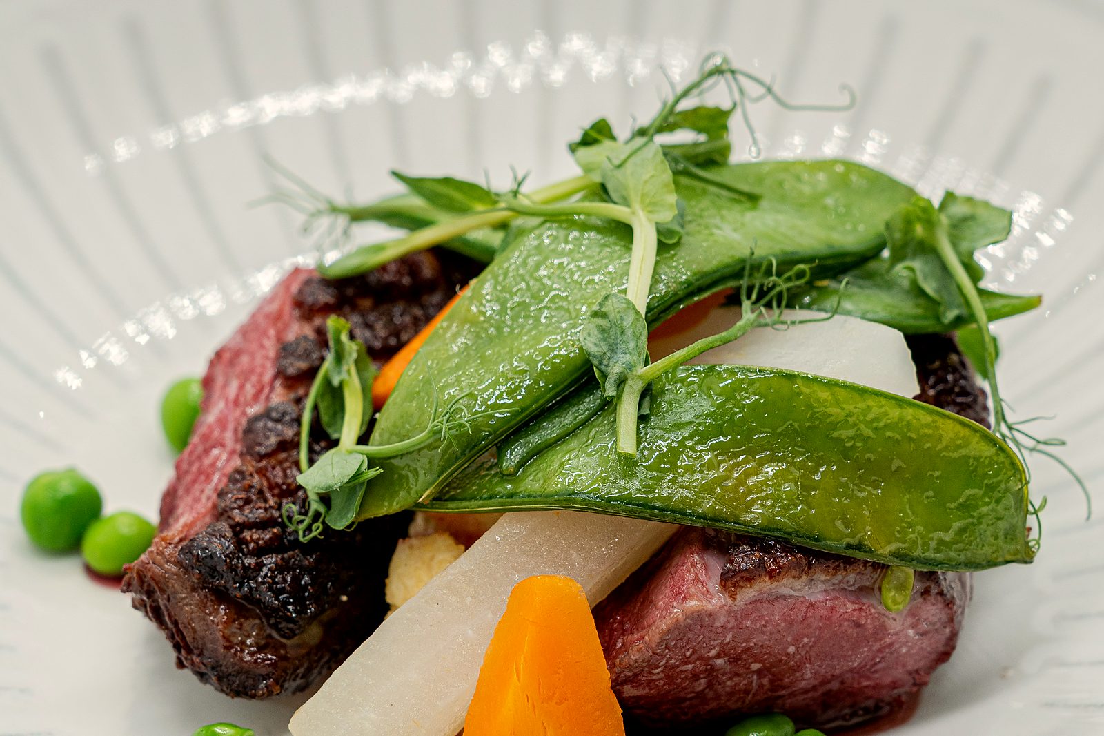 Magret rôti tranché rosé, pois gourmands, petits pois et carotte glacée, plat de cuisine française du chef Anthony Boucher au restaurant L’Apibo, Paris 2e