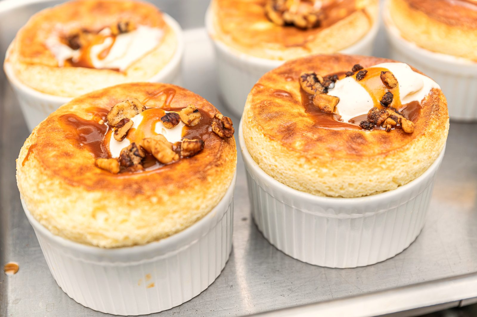 Soufflés dorés aux noix caramélisées alignés en ramequins blancs au passe de la cuisine de L’Apibo, prêts à partir en salle rue Tiquetonne